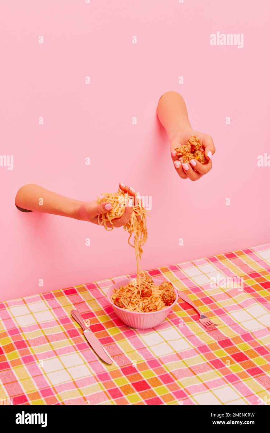 Food pop art photography. Female hand sticking out pink paper and holding spaghetti and meatballs. Dinner time Stock Photo