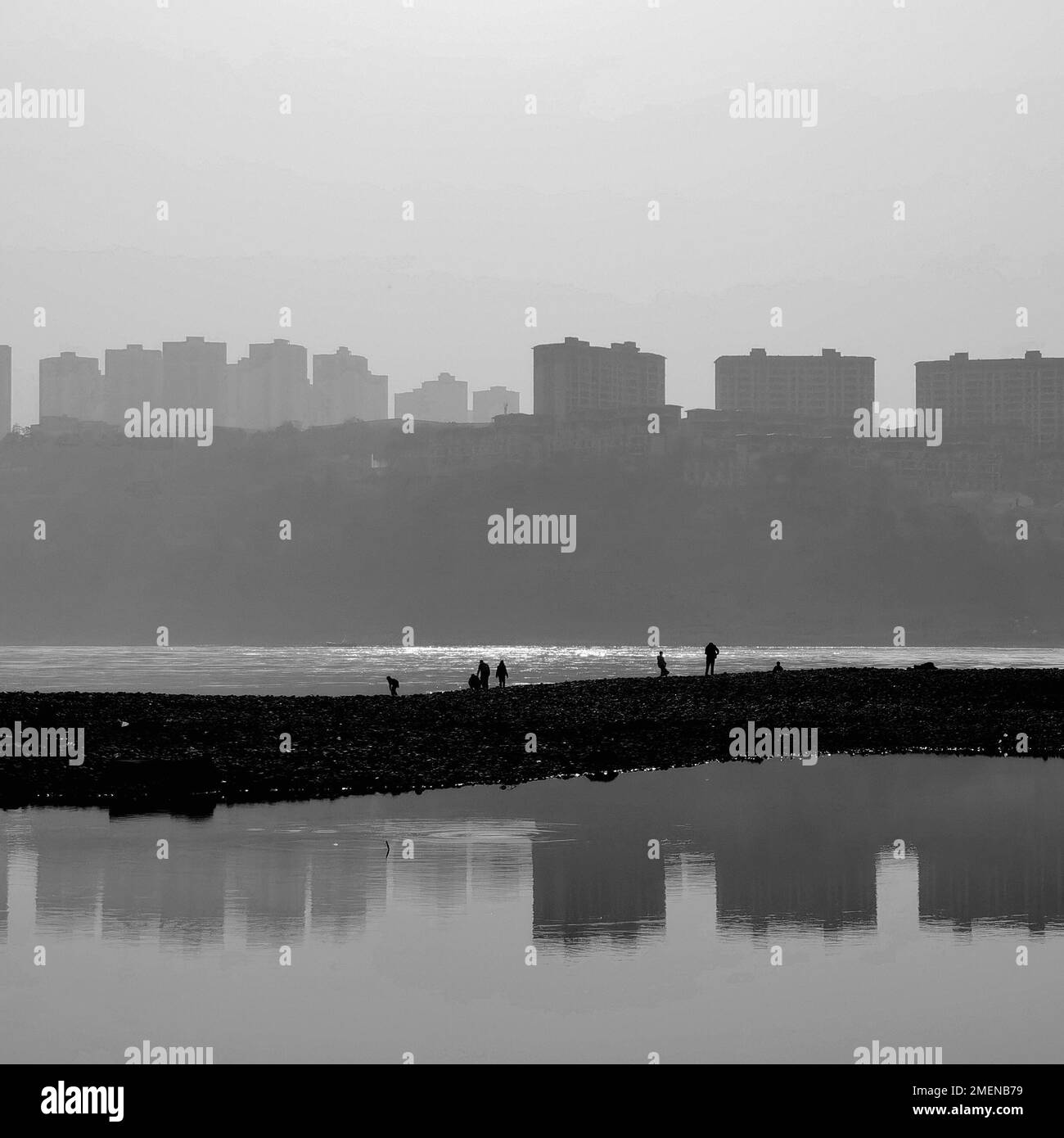 A grayscale shot of the Yangtze river with silhouettes of people and city buildings. Stock Photo