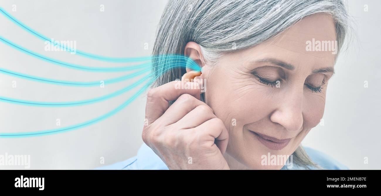Mature woman holding hearing aid near her ear with colored sound waves showing variety of sounds going to her ear. Hearing aids Stock Photo