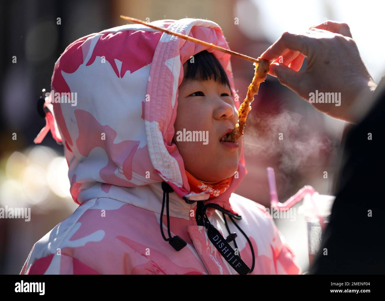 (230124) -- TANCHENG, Jan. 24, 2023 (Xinhua) -- A girl tastes food at a ancient town scenic spot of Tancheng County in Linyi City, east China's Shandong Province, Jan. 24, 2023. People enjoy various kinds of cuisine in China during the Spring Festival holiday. (Photo by Zhang Chunlei/Xinhua) Stock Photo