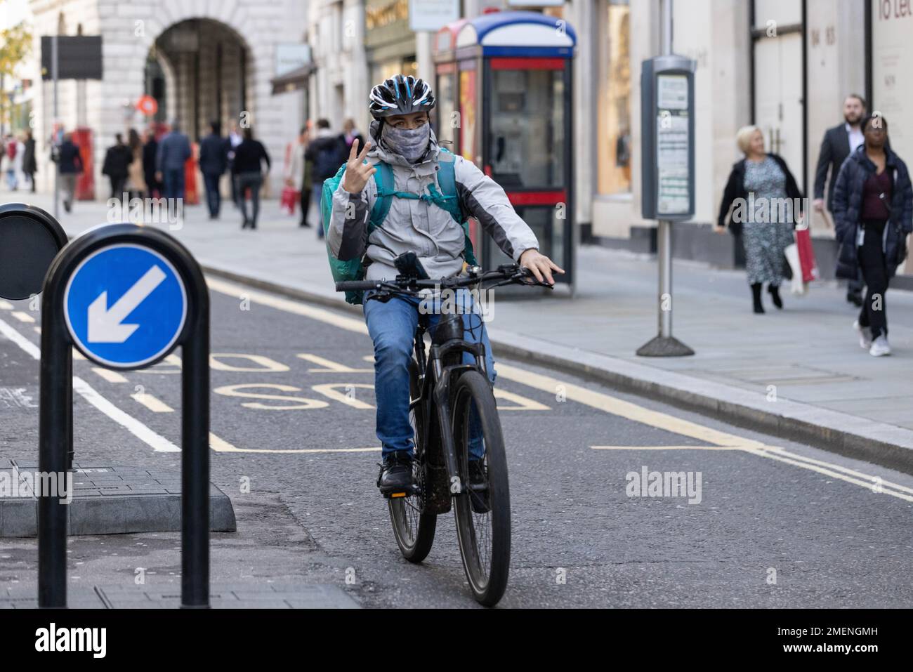 UBER delivery cyclist making a rude gesture using his two fingers as he cycles along a busy road in the City of London, England, United Kingdom Stock Photo