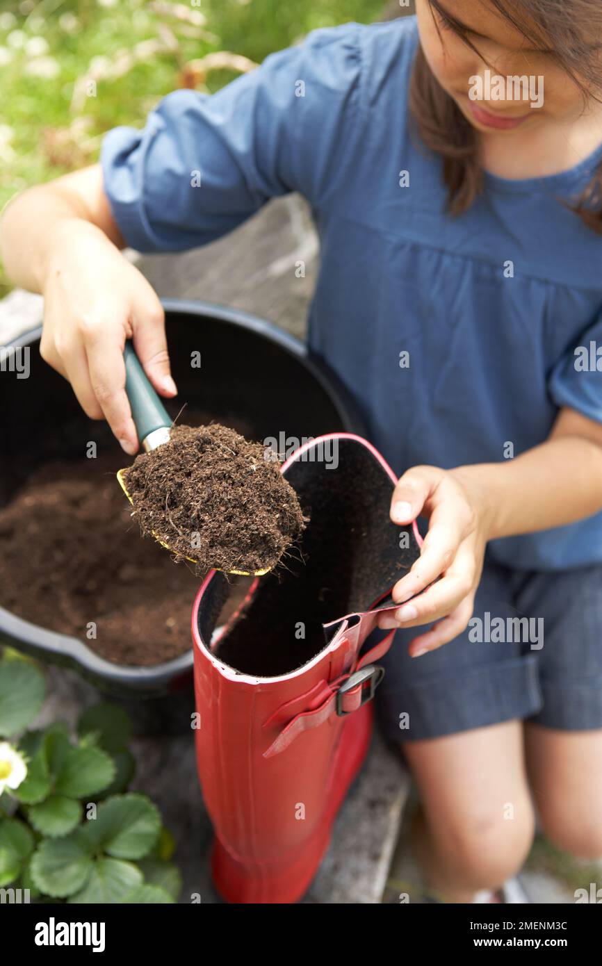 strawberry, young girl filling red welly up with soil Stock Photo
