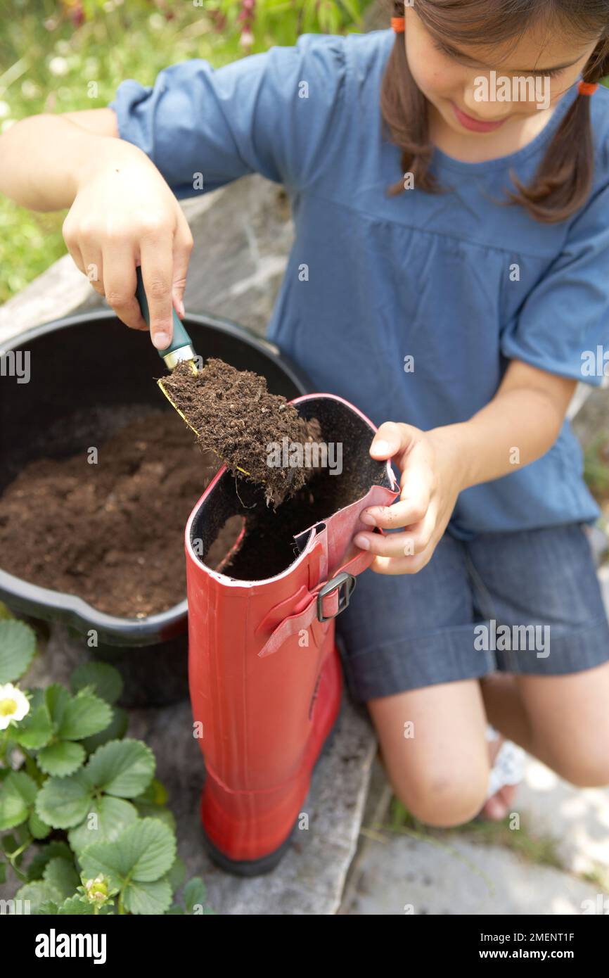 strawberry, young girl filling red welly up with soil Stock Photo
