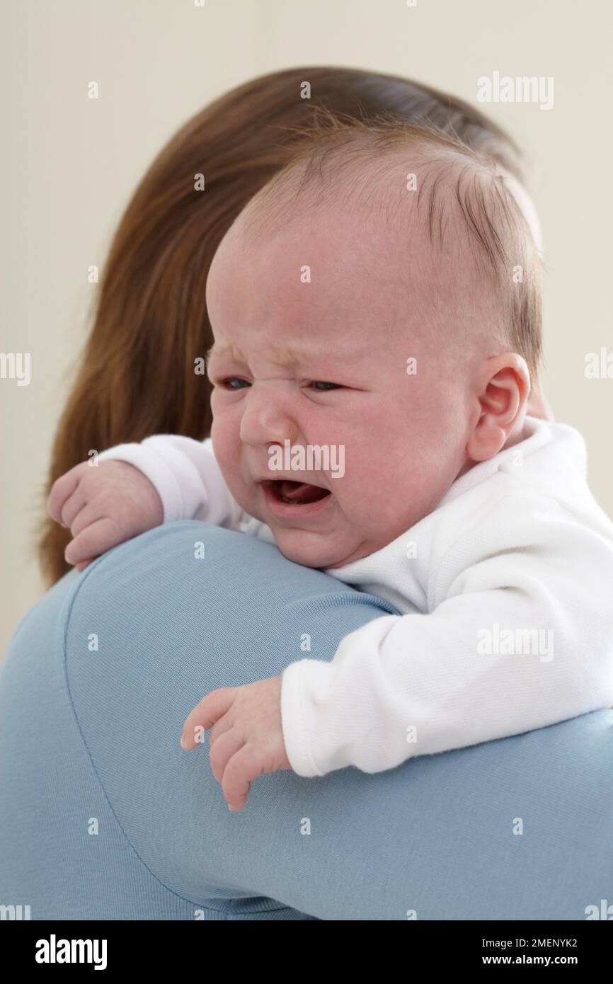 Mother holding crying baby boy (9.5 weeks) against her shoulder, close-up Stock Photo