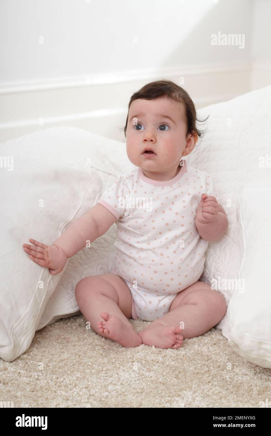 Baby girl (6 months) sitting on floor supported by cushions, front view