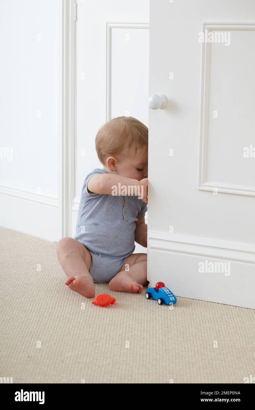 Baby boy (12 months) sitting on carpet and opening cupboard door Stock