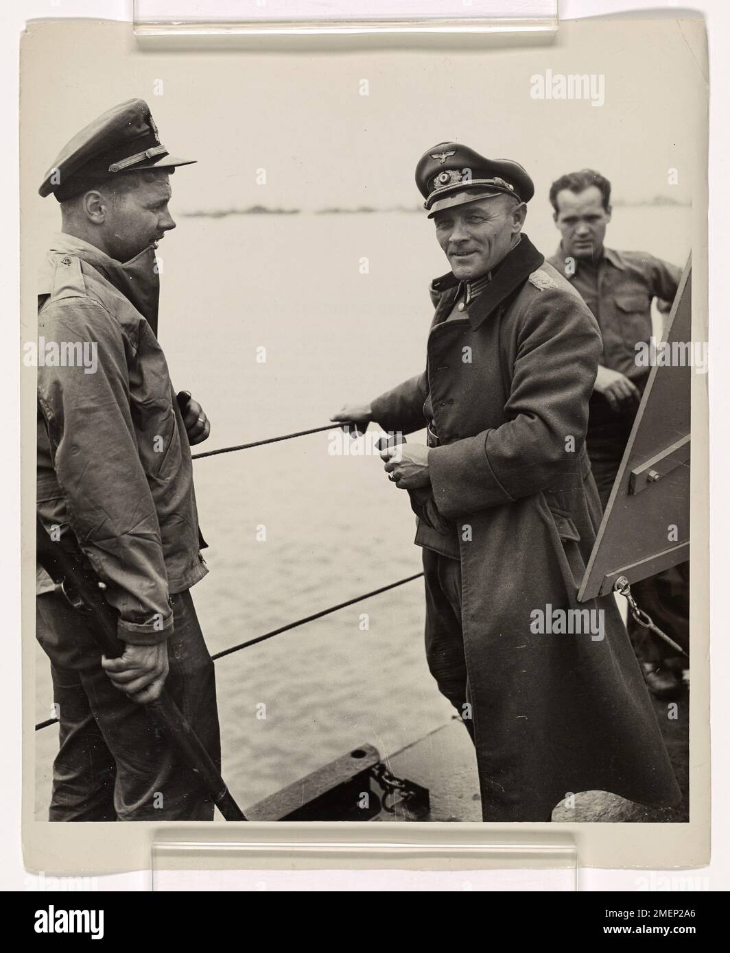 Photograph of Nazi Lieut. Col. Hans Franz Muller (right) Talking With Coast Guard Ensign Axel B. Carlson as the German Is Transported Across the English Channel for Internment in England. Beribboned Nazi Officer Captured at St. Lo. Aboard a Coast Guard-manned LST, Nazi Lieut. Col. Hans Franz Muller (right), four times decorated for his war exploits, talk with Coast Guard Ensign Axel B. Carlson as the German is transported across the English Channel for internment in England. Muller was captured in the battle of St. Lo. He wears the Iron Cross and other medals and a ribbon for participation in Stock Photo