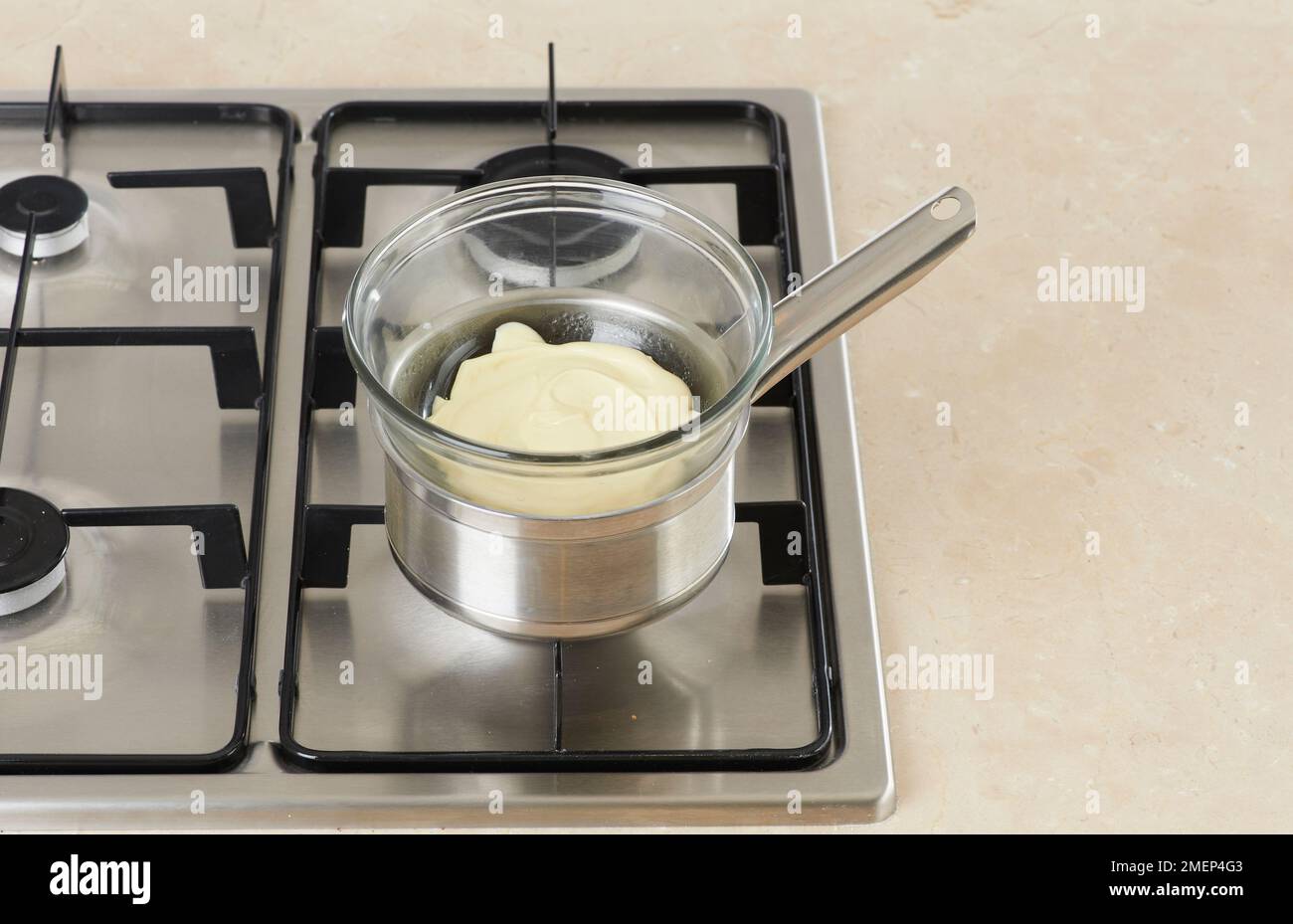 Melting white chocolate in bowl place over pan of boiling water Stock