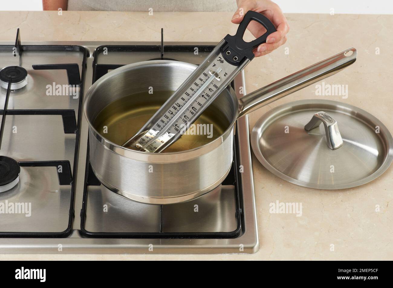 Heating oil in pan and checking temperature with thermometer Stock Photo
