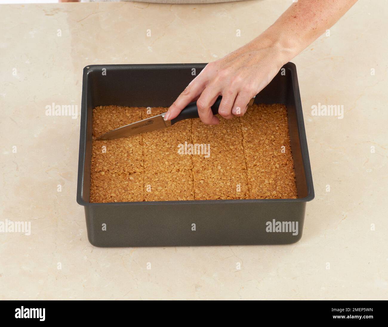 Using kitchen knife to slice flapjacks in baking tin Stock Photo Alamy