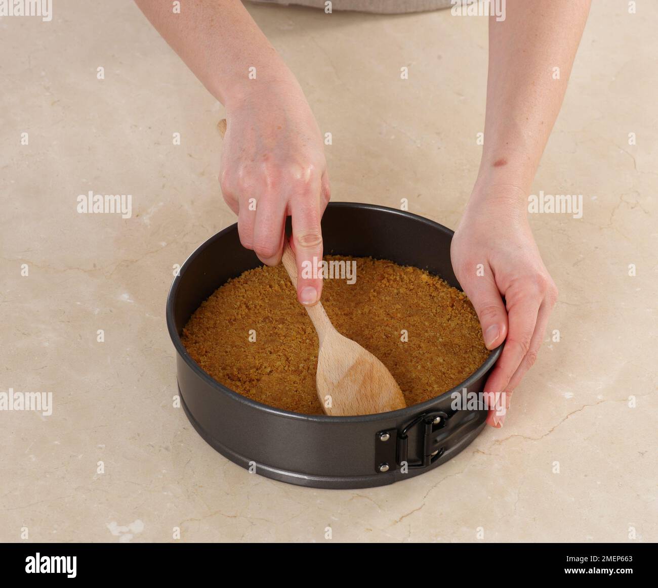 Pressing crushed biscuits mixture into base of cake tin using wooden
