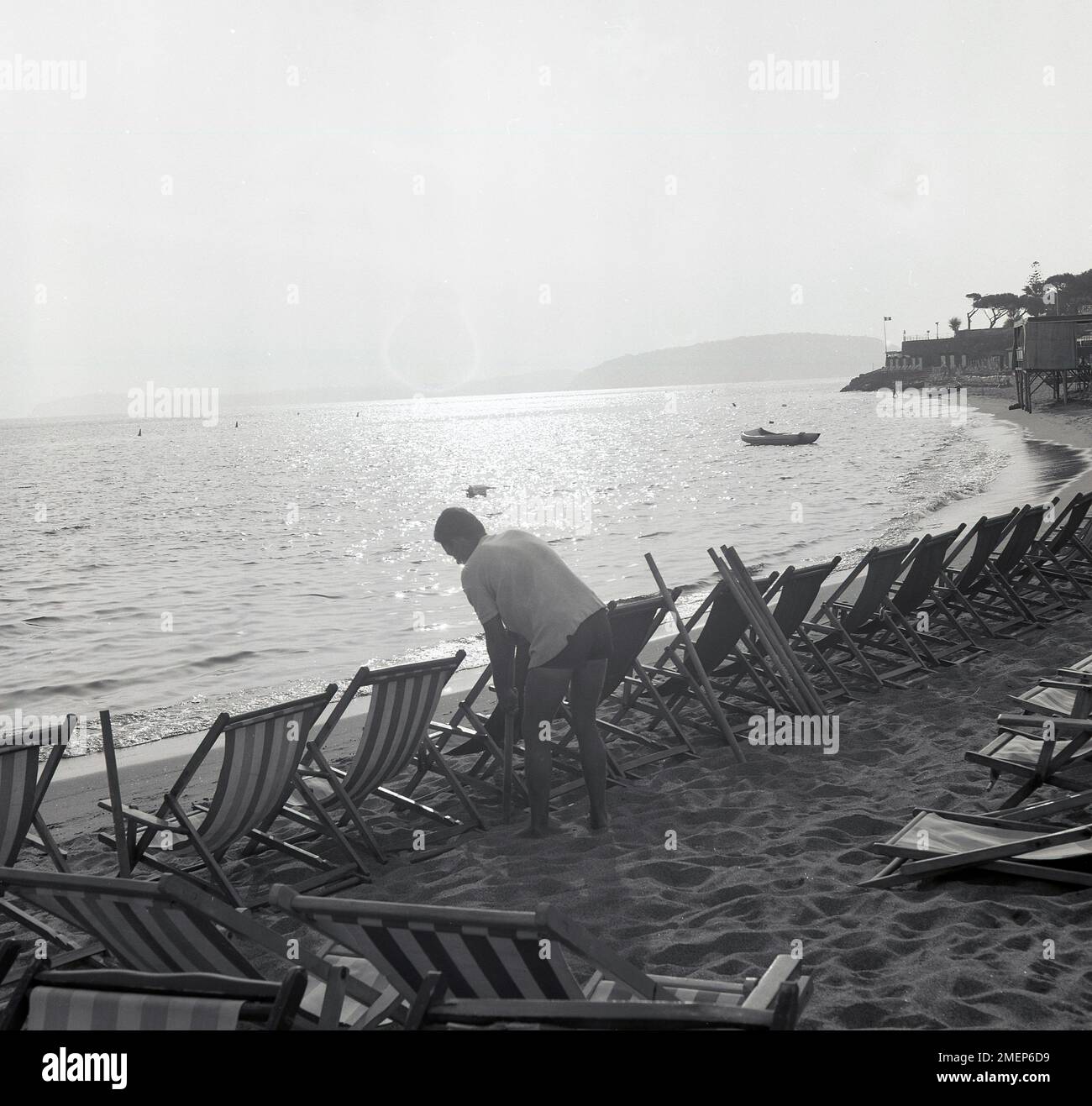 1960s, historical, early morning and a male attendant putting wooden poles down beside deckchairs on the beach on the Island of Ischia, Italy. Stock Photo
