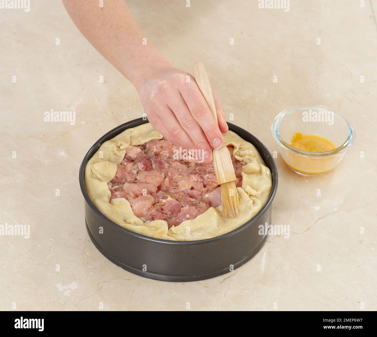 Chicken and Ham Raised Pie, brushing edges with egg glaze Stock Photo