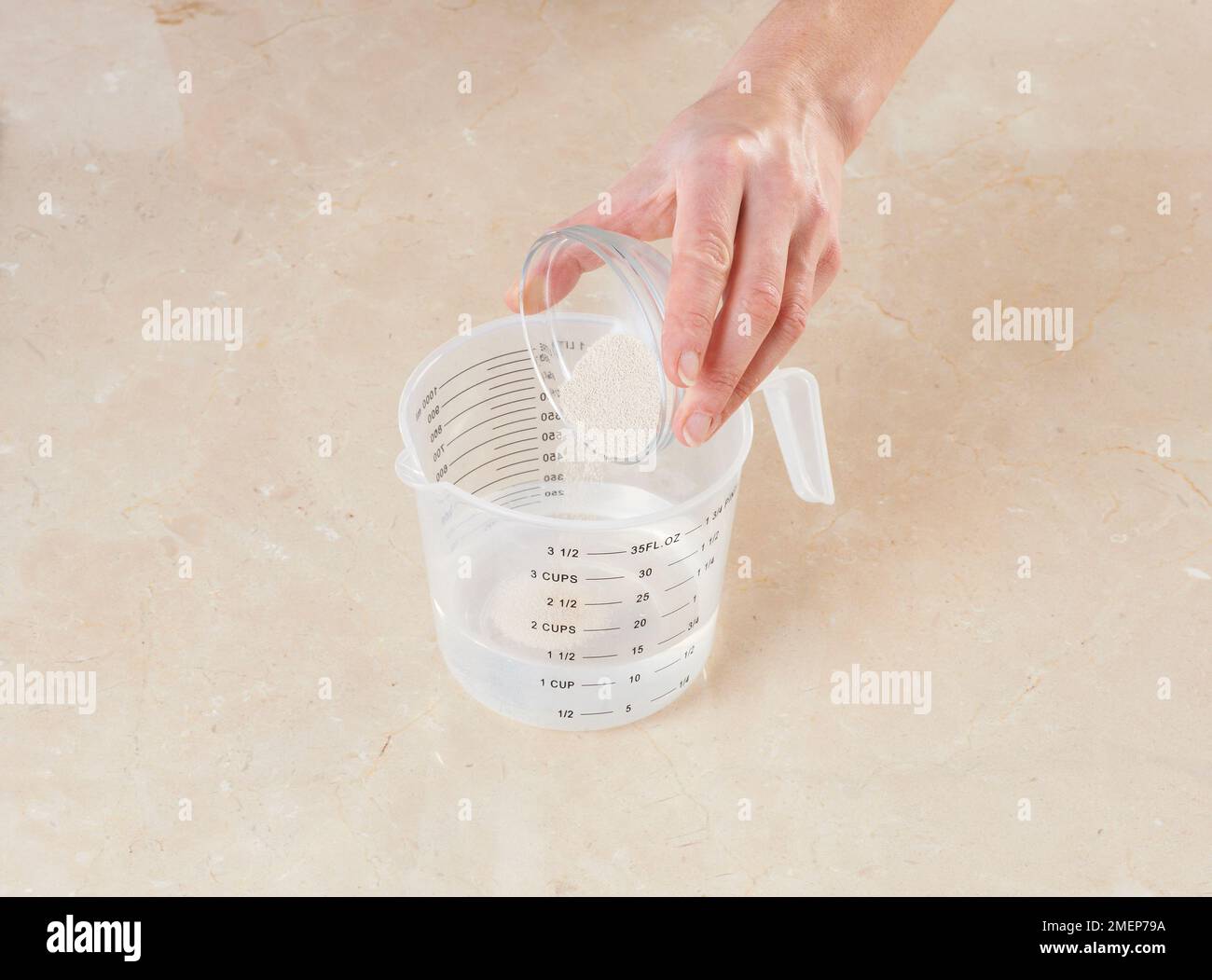 Emptying dry yeast into measuring jug containing water Stock Photo