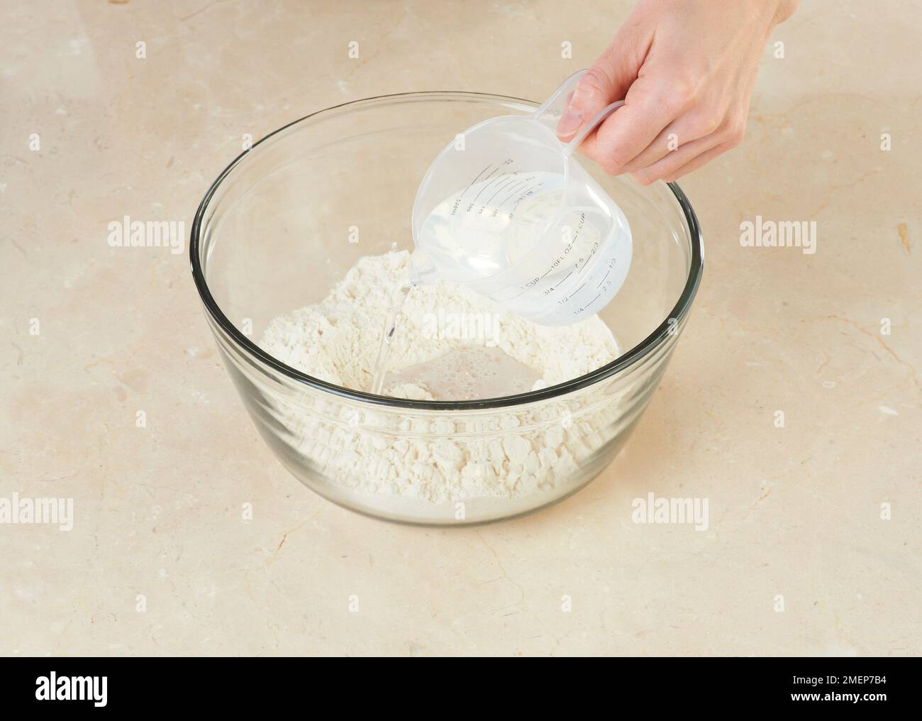 Pouring water onto flour in glass mixing bowl Stock Photo Alamy