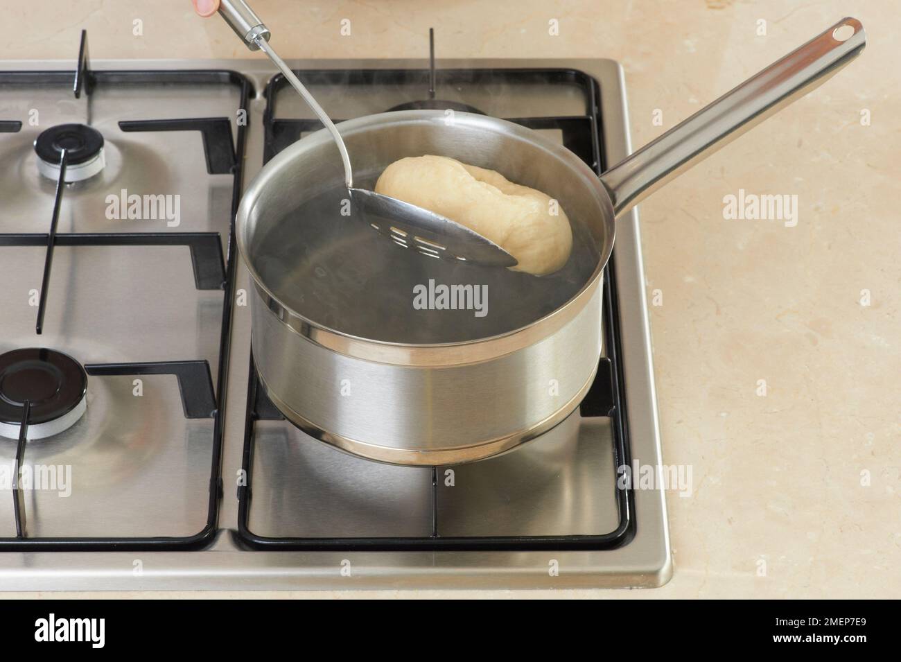 Using slotted spoon to remove bagel from saucepan of boiling water on