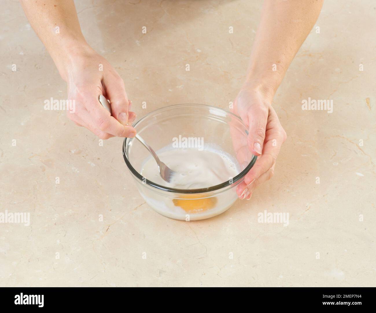 Using fork to whisk yeast and egg yoke in glass mixing bowl Stock Photo
