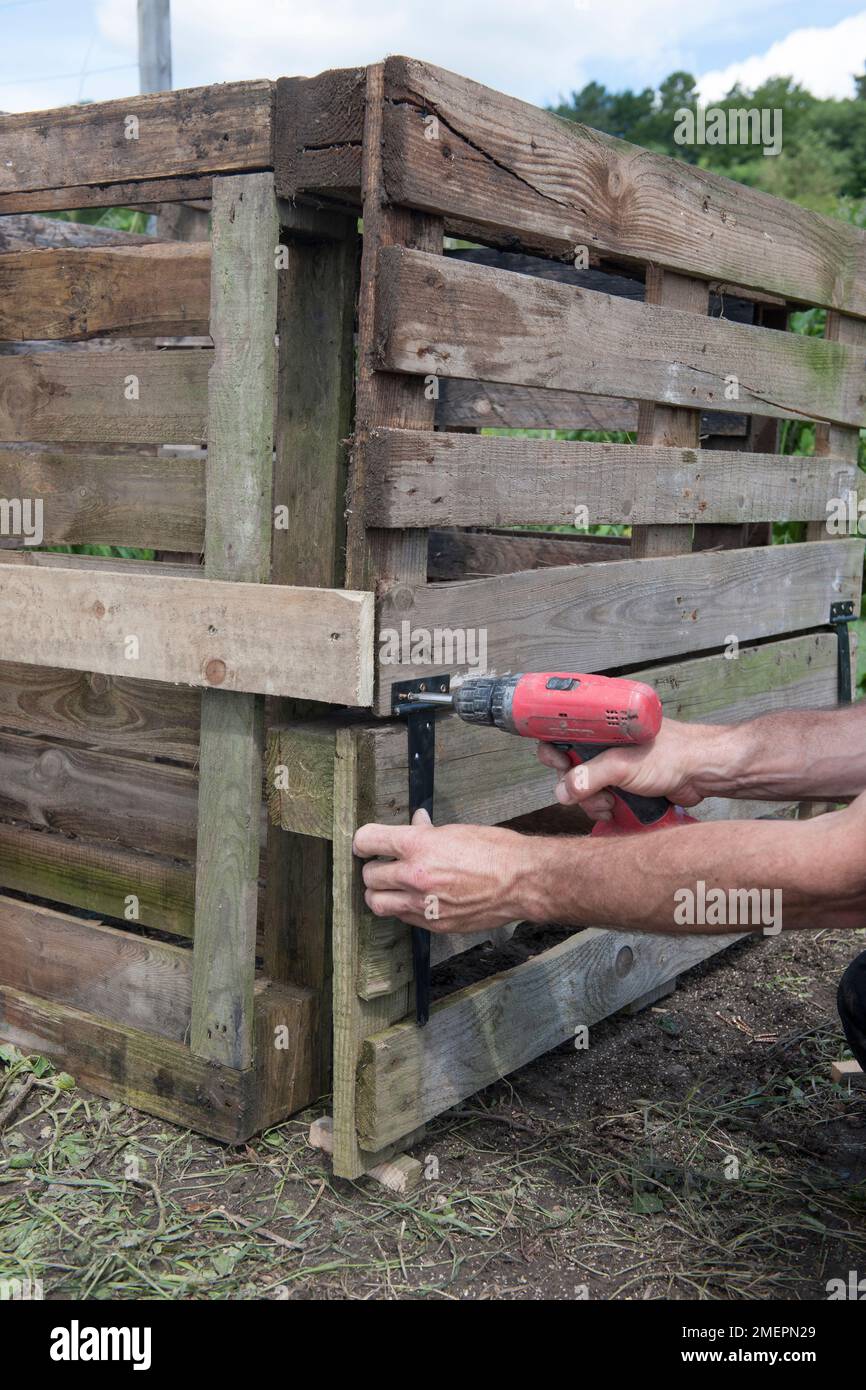 Man constructing compost heap out of wooden pallets and creating a