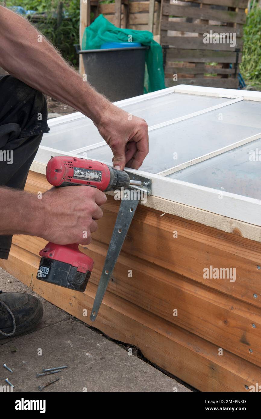 Man constructing a cold frame with a drill Stock Photo