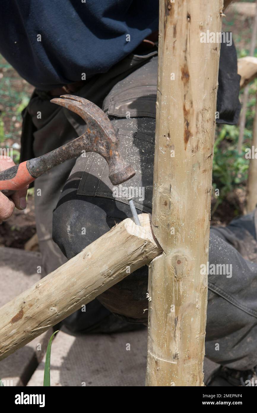 Man using hammer and nail to fit support to fence post Stock Photo Alamy