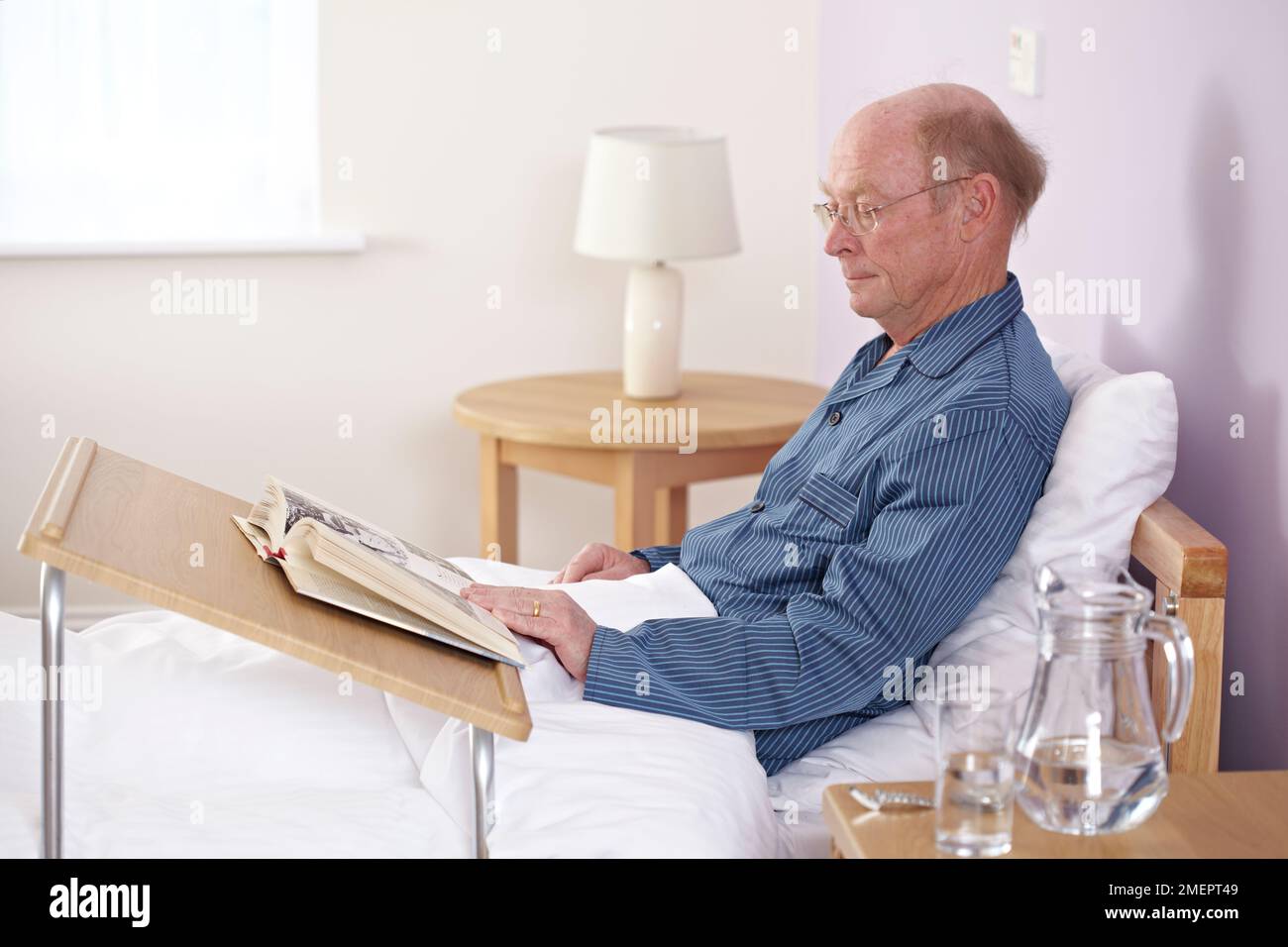 Man sitting up in bed reading a book, using portable table or overbed