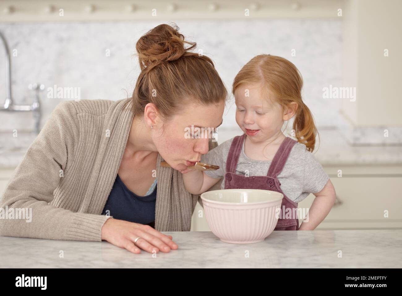 Girl spooning liquid out of bowl and offering to woman to eat, 2 years