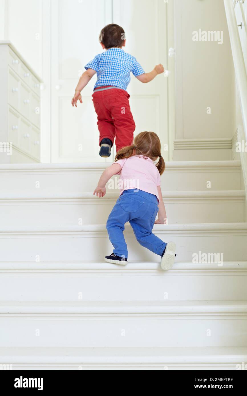 Boy running at top of stairs followed by young girl, 2 years Stock Photo