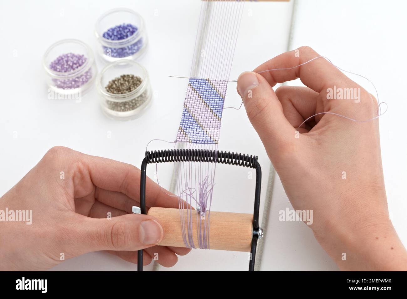Making a loom-woven bead cuff, adding new weft thread with needle, close-up Stock Photo
