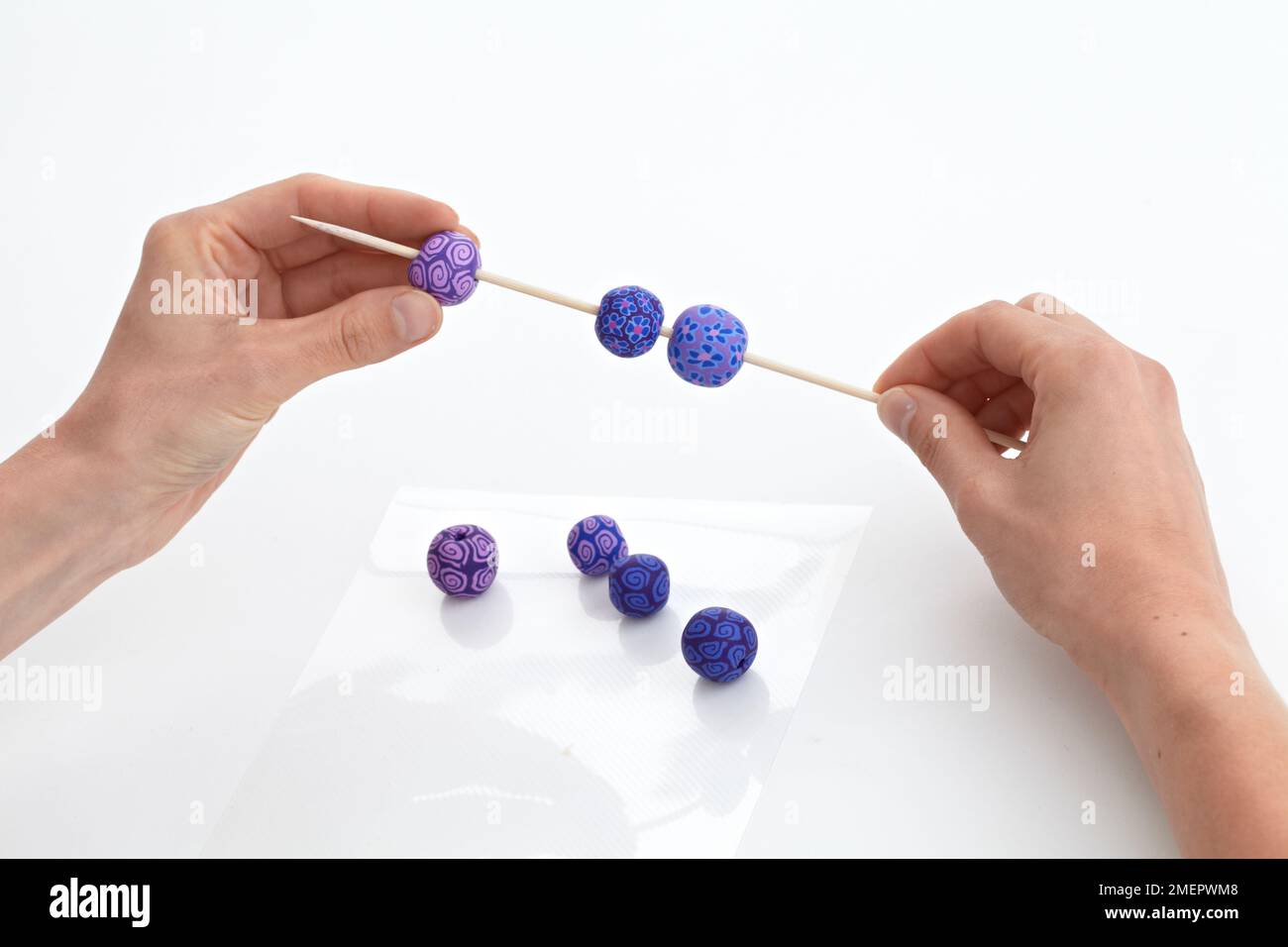 Threading polymer clay beads onto wooden skewer, close-up Stock Photo