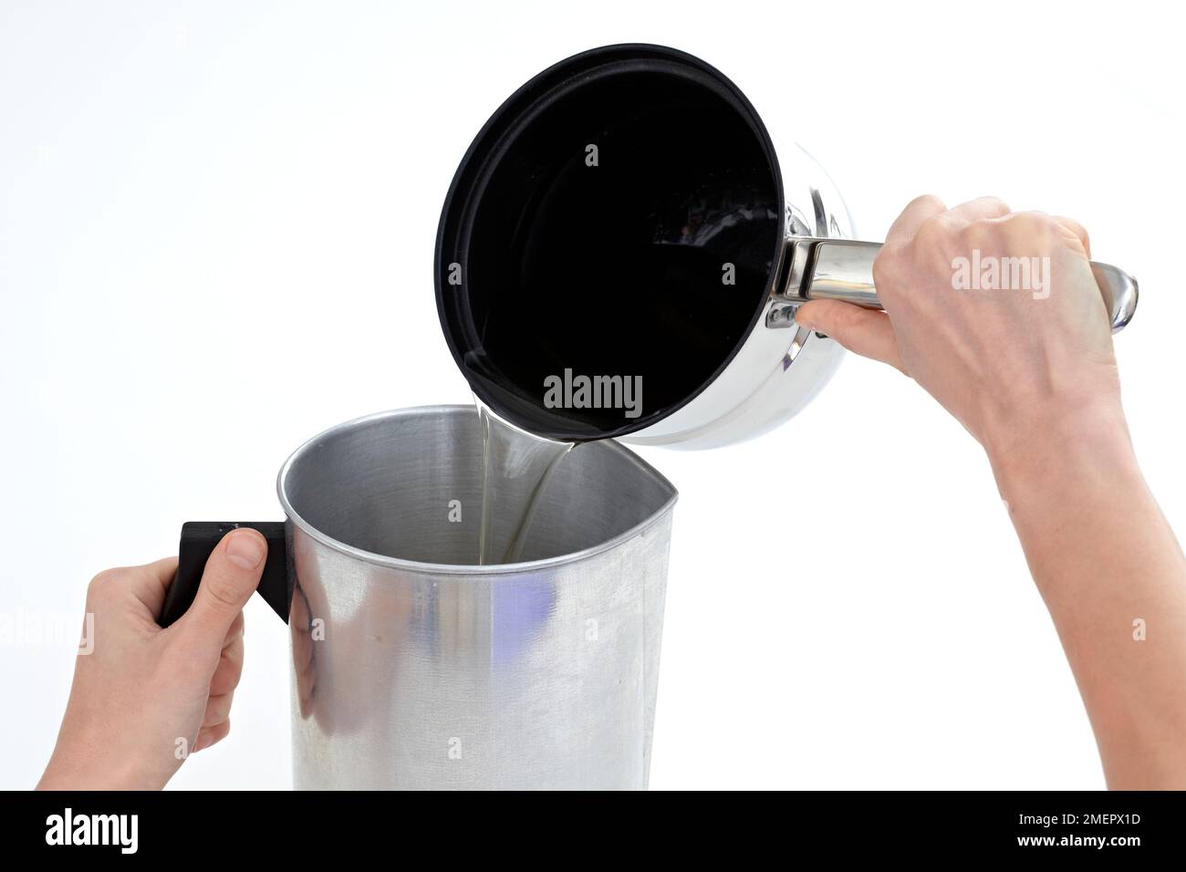 Pouring melted soy wax from double-boiler into metal jug to make three-layer candle, close-up Stock Photo