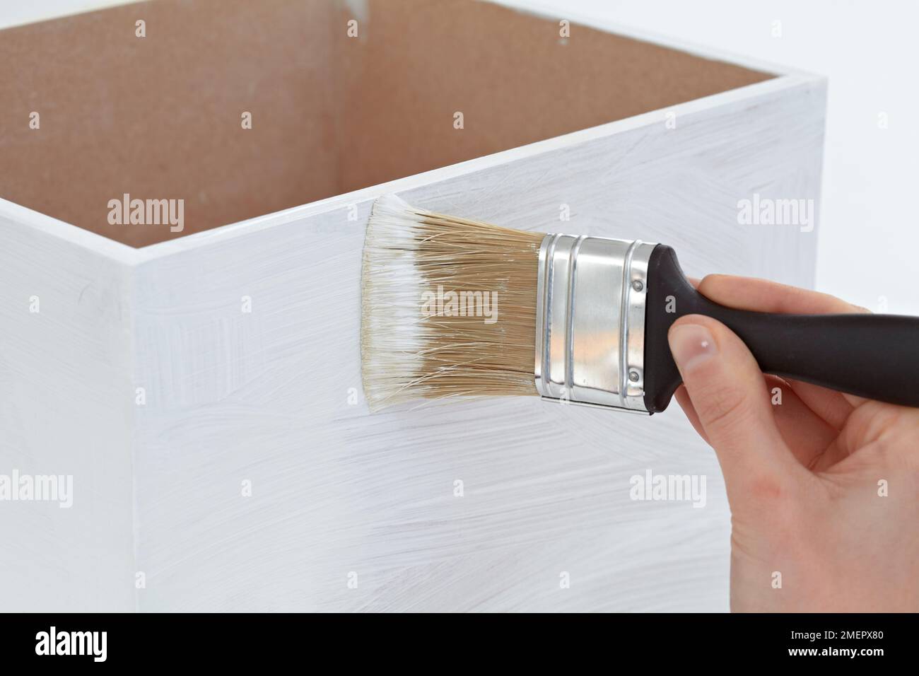 Woman using large brush to paint white matt emulsion to primer on wooden box, close-up Stock Photo