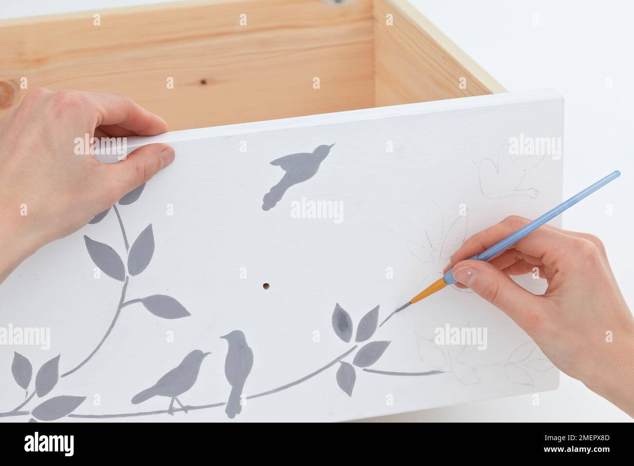 Using artists' brush to paint design on bedside drawer front