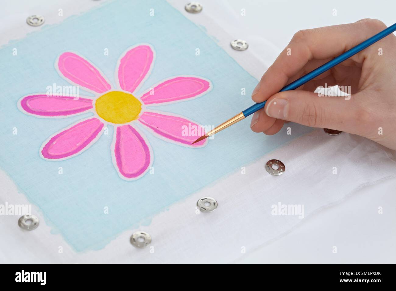 Woman using fine brush to paint in petal color of flower on batik frame, close-up Stock Photo