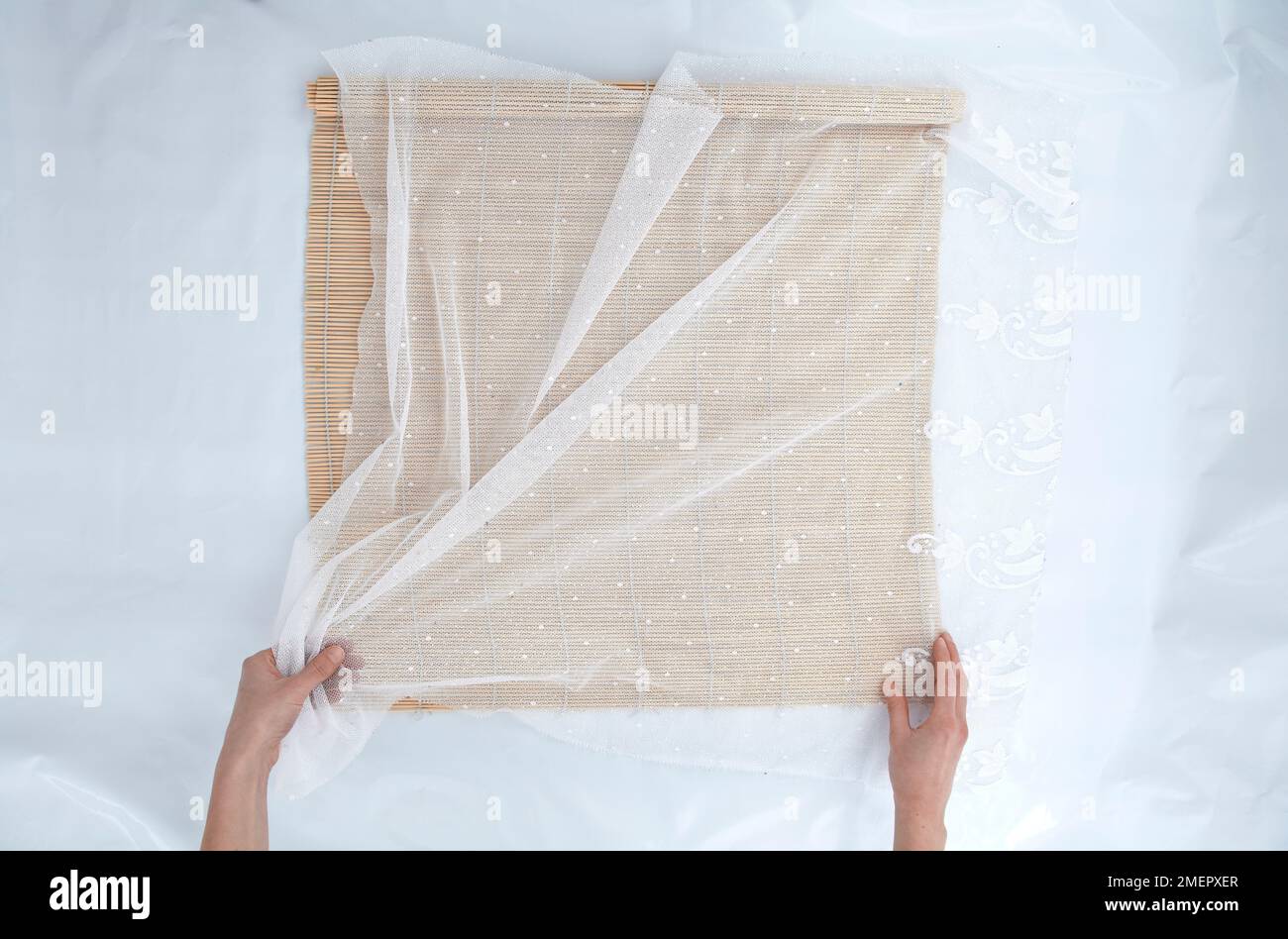 Placing net curtain on bamboo blind to prepare work surface for wet felting, overhead view Stock Photo