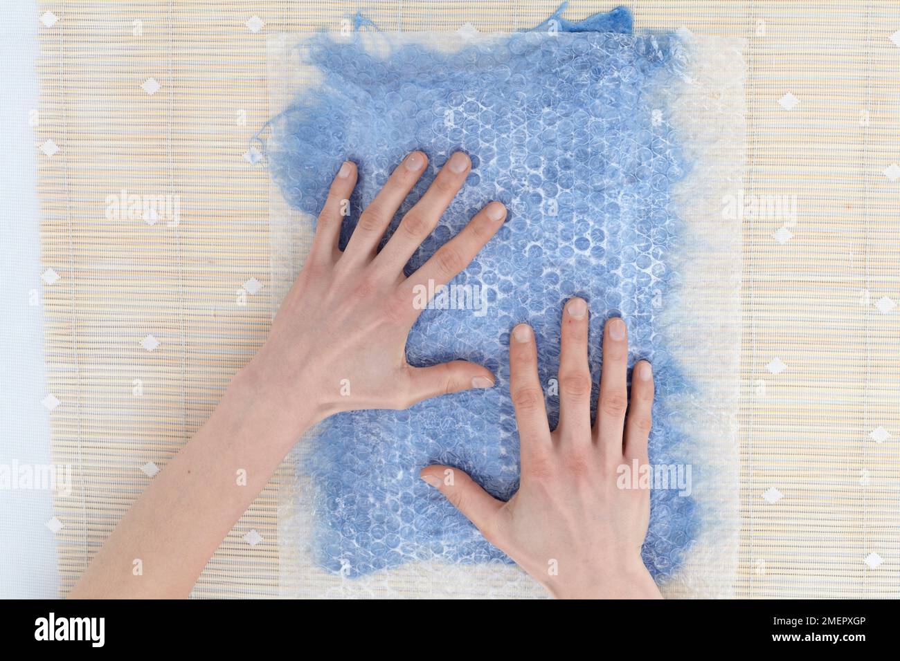 Placing sheet of bubble wrap on top of wetted fibres and use hands to spread moisture evenly across fleece, overhead view Stock Photo
