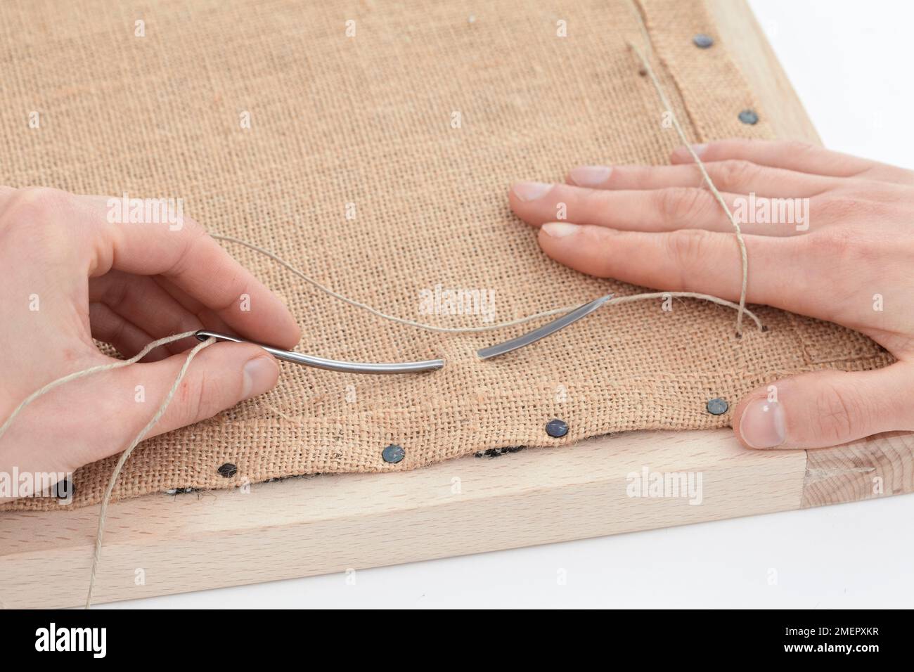 Using twine threaded through curved spring needle to apply bridle ties to upholstery hessian to make seat, close-up Stock Photo