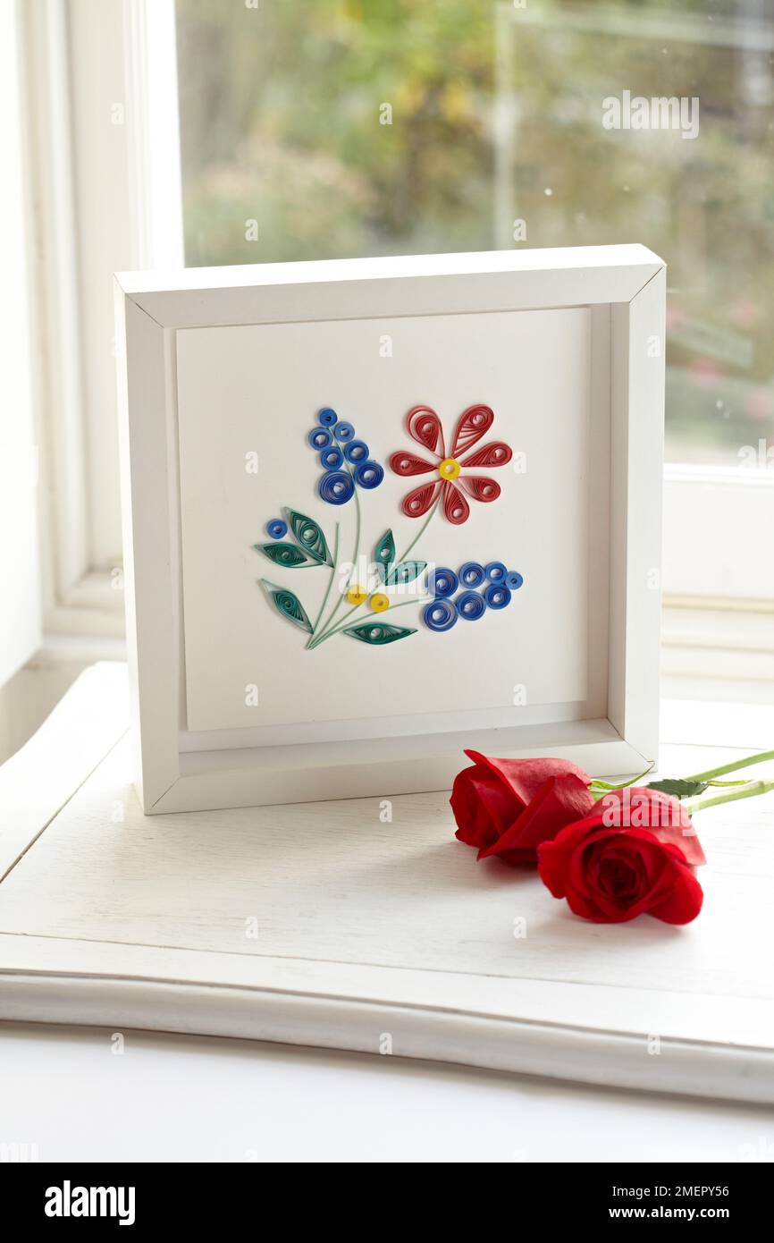 Quilled paper picture in frame with two red roses in front Stock Photo