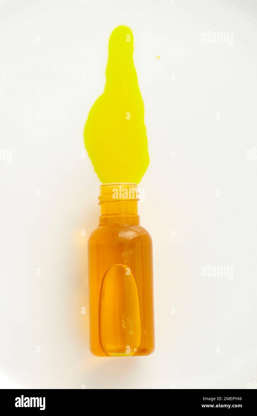 Yellow colourant liquid spilling out of small bottle, overhead view Stock Photo