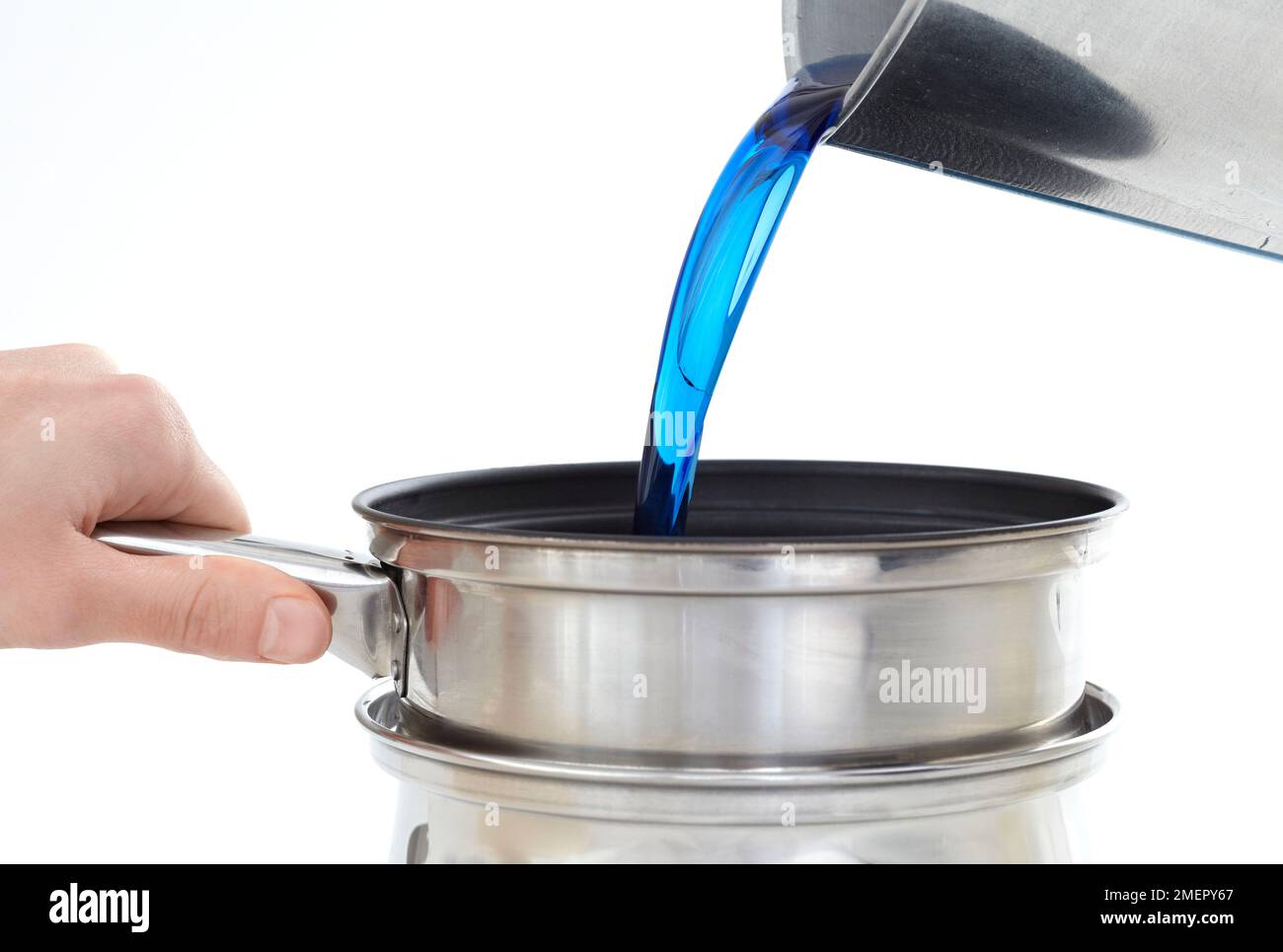 Pouring blue wax from deep saucepan into double-boiler to make three-layer candle, close-up Stock Photo