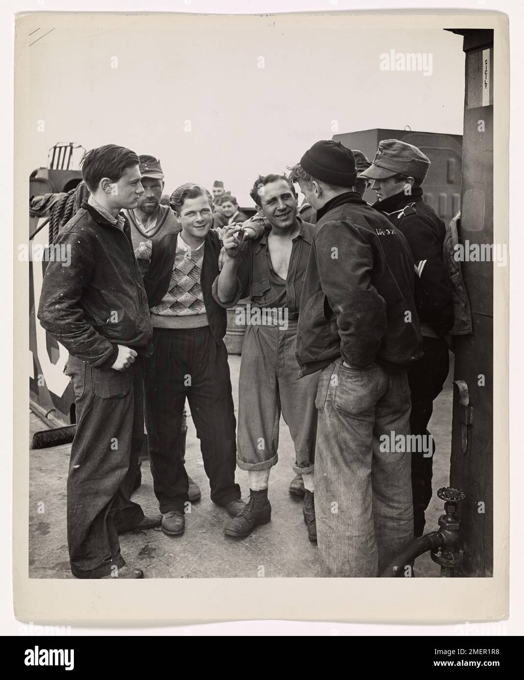 Photograph of Nazi Prisoners Chatting With Coast Guardsmen Aboard the Coast Guard-manned LCI Which Is Transporting Them from the French Coast to England and to a War Prisoner's Camp. Farewell to Arms for These Nazis. Seemingly far from displeased by their capture, Nazi prisoners chat with Coast Guardsmen aboard the Coast Guard-manned LCI which is transporting them from the French coast to England and to a war prisoner's camp. These Coast Guardsmen are: Allen Aylward (left), Radioman Third Class, of Beverly, Mass., and Harold Goodwin (right), back to camera), Signal Man Second Class of Fort Wor Stock Photo