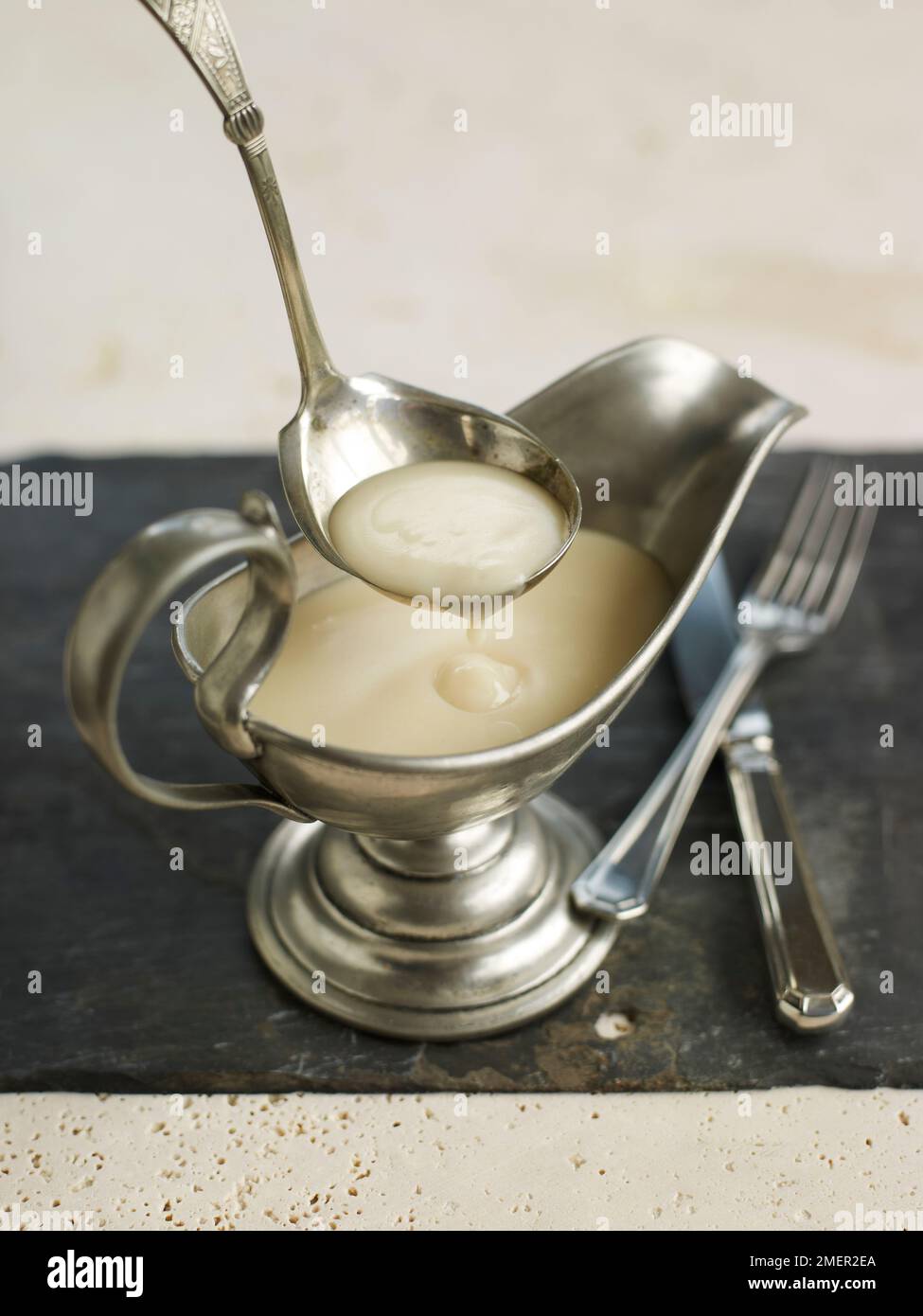 Veloute sauce in silver sauce boat and serving spoon or ladle Stock Photo