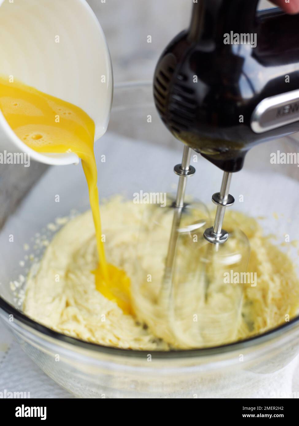 Adding eggs to Victoria sponge cake mixture in mixing bowl, using