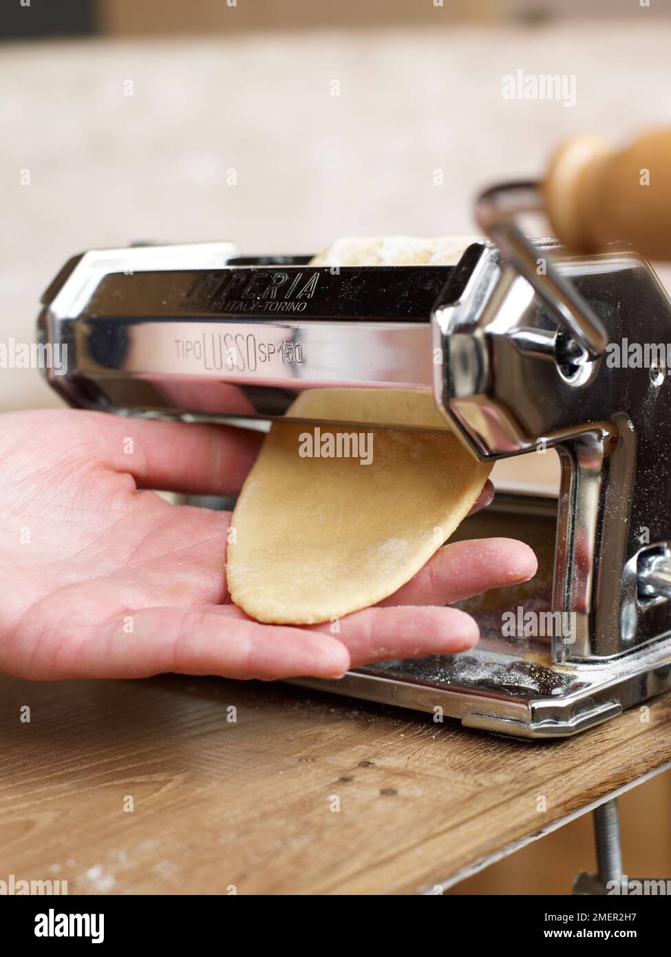 Rolling dough through pasta machine to make thin sheet Stock Photo Alamy