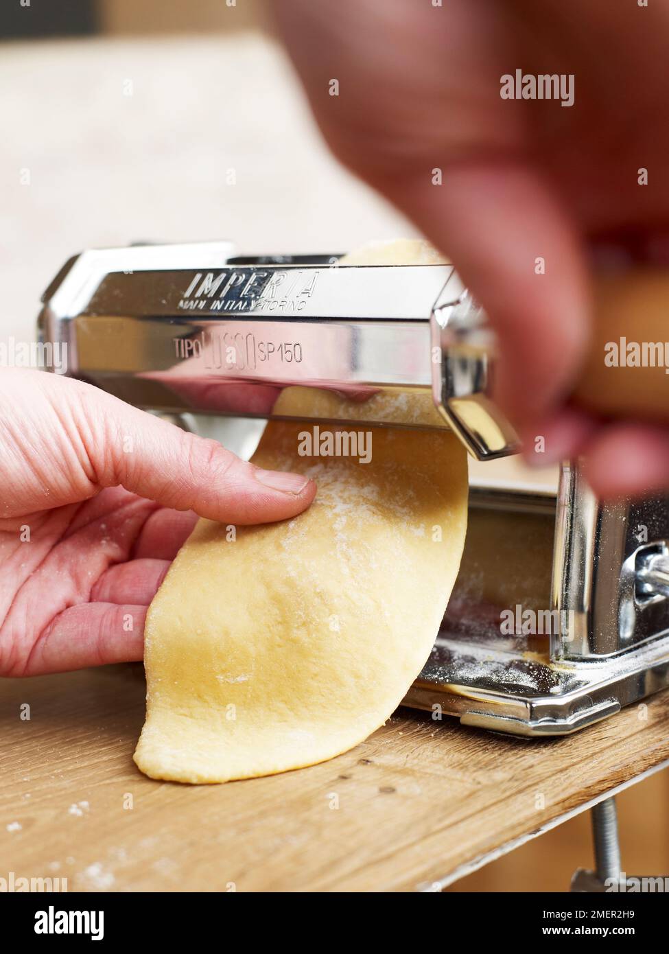 Rolling dough through pasta machine to make thin sheet Stock Photo Alamy