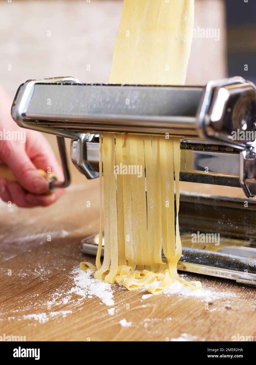 https://c8.alamy.com/comp/2MER2HA/strands-of-tagliatelle-pasta-coming-out-of-pasta-machine-2MER2HA.jpg