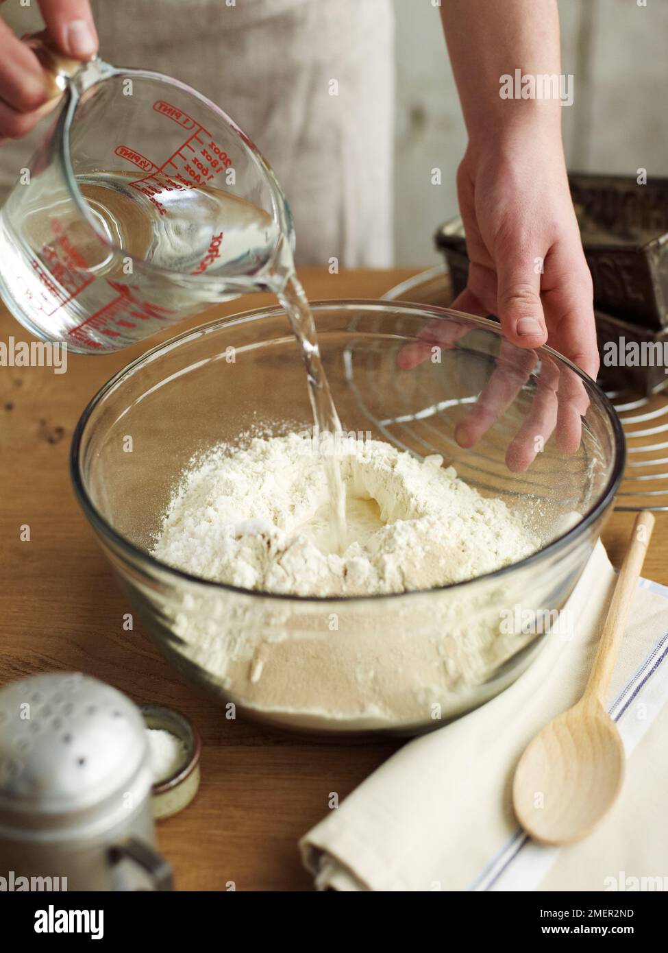 Pouring water from jug to mix with other ingredients in bowl (making bread) Stock Photo