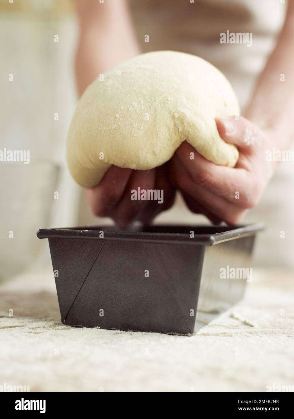 Placing kneaded and partially risen bread dough in loaf tin Stock Photo