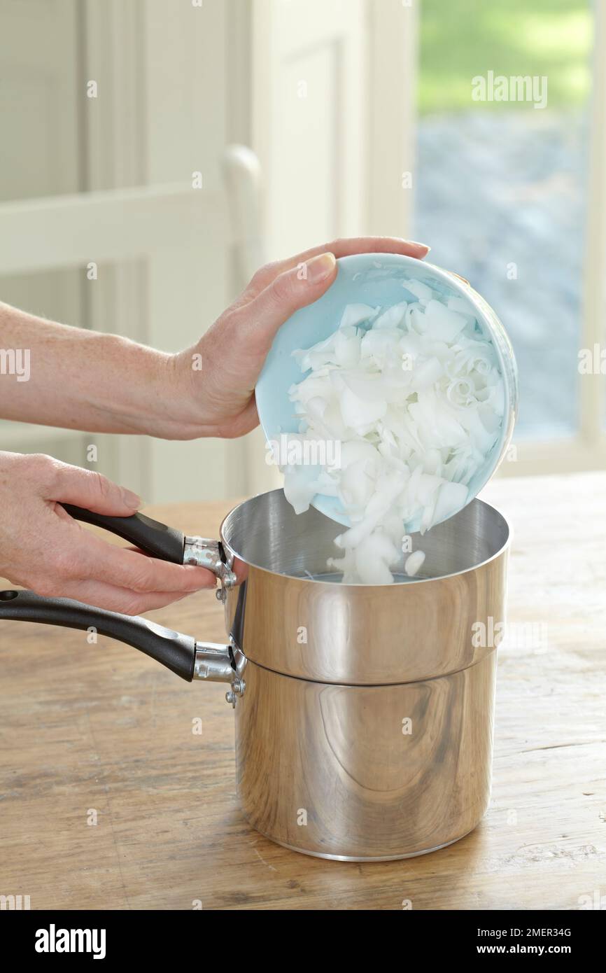Pouring wax flakes to top saucepan of double-boiler (making candles) Stock Photo