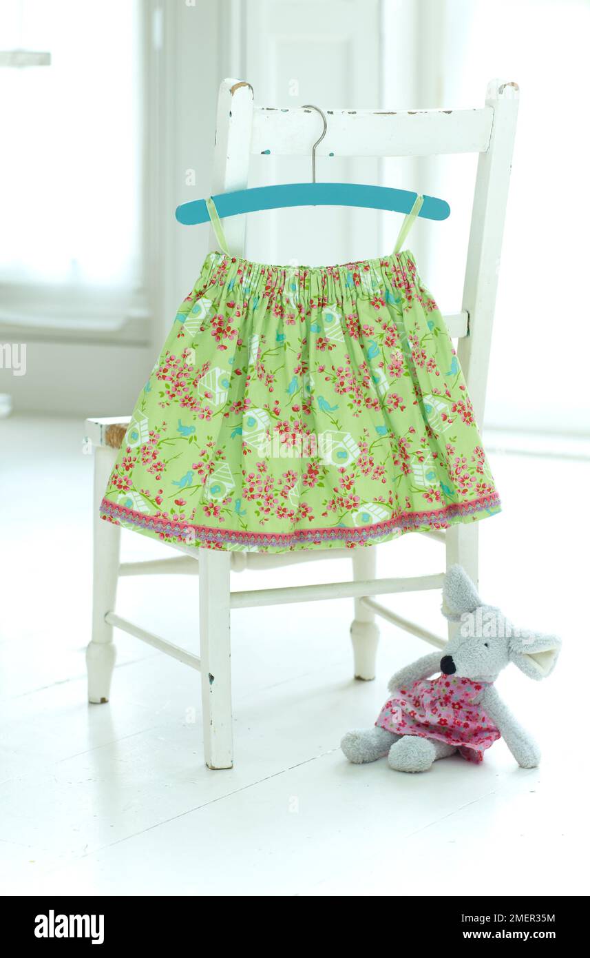Patterned, green girl's skirt hanging from chair, toy mouse in pink skirt nearby on the floor Stock Photo