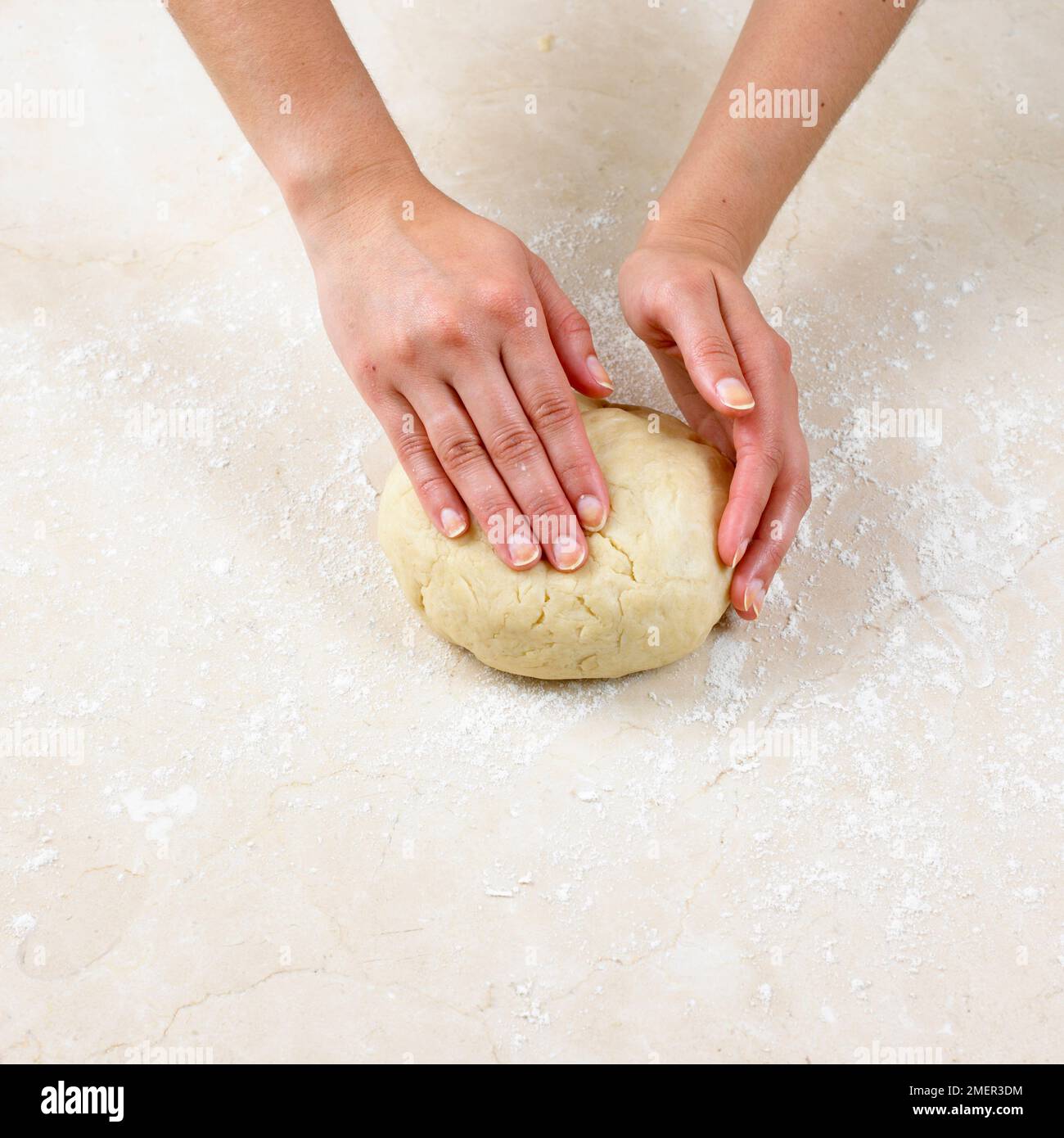 Hands gently kneading suet crust pastry ball on floured surface Stock